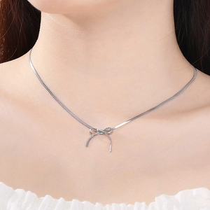 Gros plan détaillé d'un collier avec pendentif nœud argenté et chaîne plate fine
