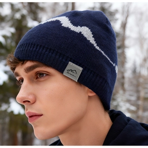 Detail of navy knit beanie featuring peak pattern and logo patch in snowy forest