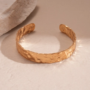 Detailed view of golden cuff bracelet featuring irregular hammered metal texture and open design