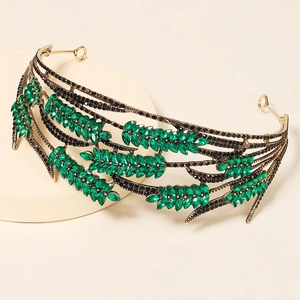 Elegant gold crown with green leaf rhinestones and black crystals on a beige pedestal
