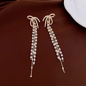 Detailed view of golden bow earrings featuring sparkling zircon and long pearl tassels