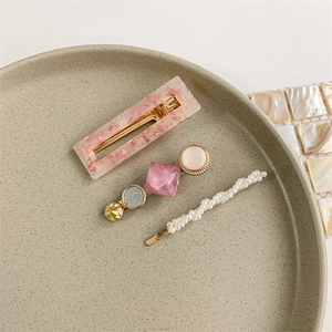Detailed set of three elegant pearl and floral acrylic hair clips on ceramic tray