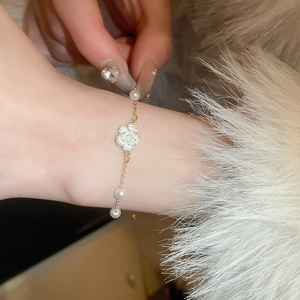 Détail de bracelet camélia et perles dorées avec strass sur manche en fourrure