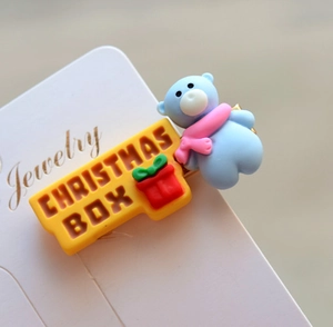 Macro view of a resin Christmas bear hair clip with a festive gift box on a jewelry card