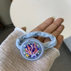 Close-up of blue fabric hair tie with round pendant featuring coral and starfish patterns