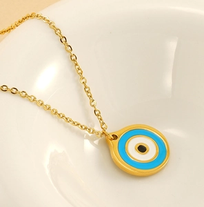 Detailed macro shot of a gold evil eye pendant necklace on a minimalist white ceramic tray