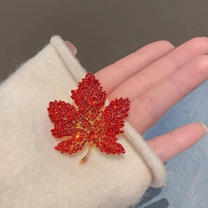 Exquisite red maple leaf brooch with red crystals on gold metal, held in hand