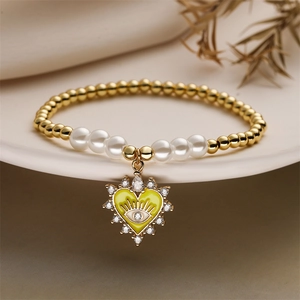 Detail of evil eye heart charm bracelet with gold beads and white pearls on ceramic tray