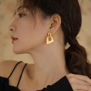 Detailed side view of matte gold irregular geometric hollow drop earrings on model