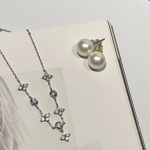 Detailed close-up of 925 silver clover necklace and pearl earrings on a book page