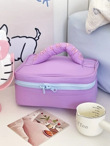 Detail of purple quilted cosmetic bag with soft ruffled handle and pink embroidered letters