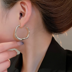 Close-up of irregular twisted silver hoop earrings worn by a model in a minimalist style