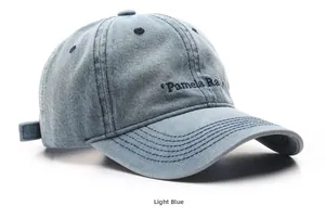 Detail of light blue washed denim baseball cap with navy blue Pamela Ra embroidery