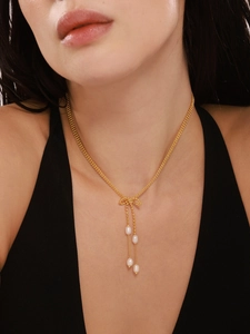 Gros plan d'un collier nœud doré avec trois perles sur le cou d'un modèle