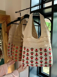 Close-up of knit tote bag featuring red floral embroidery and beige woven strap details