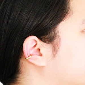 Close-up of a gold geometric C-shaped ear cuff on a model showing faceted metal design