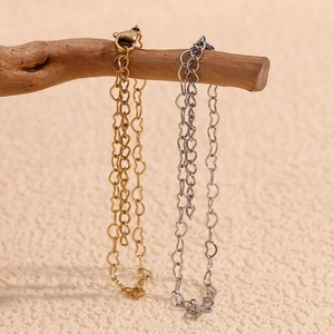 Close-up of heart chain bracelets in gold and silver finish hanging on wooden branch