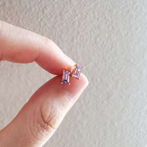 Macro shot of minimalist gold studs with rectangular purple cubic zirconia in 4-prong setting
