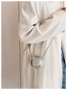 Close-up of silver mini hardshell chain bag with vertical groove texture on a beige coat