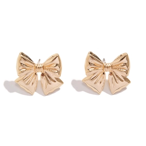 Close-up of golden bow stud earrings with detailed vertical ribbon texture and polished finish