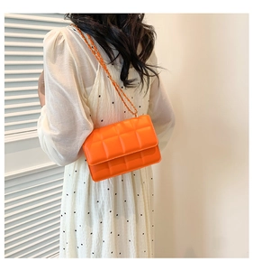 Detail of orange quilted crossbody bag with gold chain strap worn by a woman