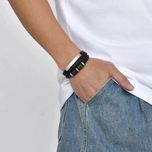 Détail d'un bracelet multicouche en cuir tressé avec breloques en argent porté au poignet