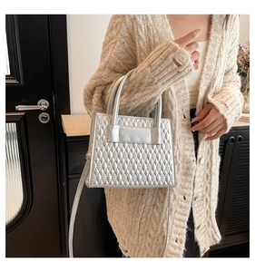 Détail d'un sac à main argenté matelassé avec poignée supérieure sur un cardigan beige