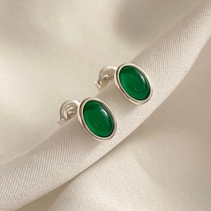 Close-up of green agate stud earrings with silver base on white textured fabric