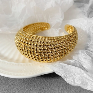 Detailansicht eines breiten goldenen Armreifs mit feiner Kugelstruktur auf einer Schale