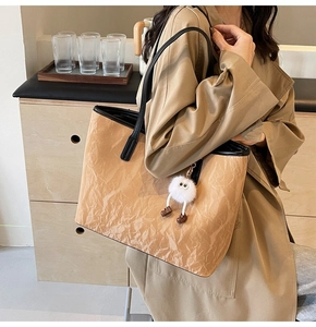 Dettaglio della borsa tote kaki con trama stropicciata e ciondolo in peluche bianco