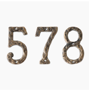 Detail of vintage bronze numbers 5, 7, and 8 with hammered iron texture and screw holes