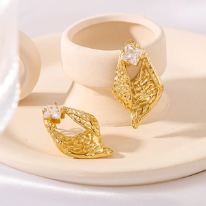 Irregular gold textured earrings with square gemstones on a ceramic tray display