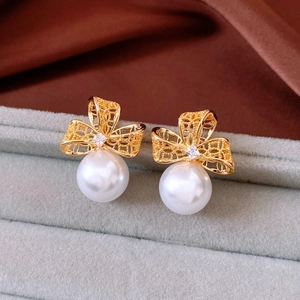 Detailed close-up of gold hollow bow earrings with shiny zircon and white pearls