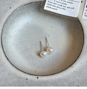 Macro shot of white freshwater pearl earrings on a textured ceramic dish