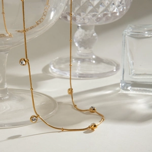 Elegante goldene Schlangenkette mit runden Zirkonia-Anhängern auf Glas-Hintergrund