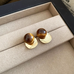 Macro shot of 18k gold plated bird earring with brown tigers eye stone on beige velvet