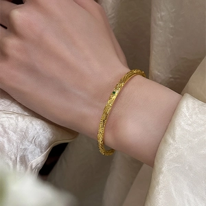 Vintage gold textured bangle with a green gemstone on elegant cream silk background