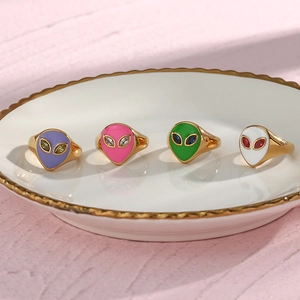 Detail of four gold alien rings with purple pink green and white enamel on a plate