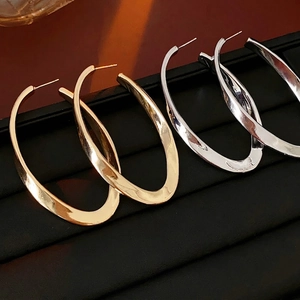 Twisted oval metal hoop earrings in gold and silver finish on black leather stand