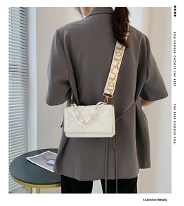 Detail of white quilted crossbody bag with luxury patterned strap and metallic chain detail