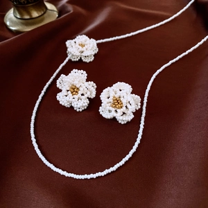 Detailed set of bead-woven camellia flower necklace and earrings on brown silk fabric