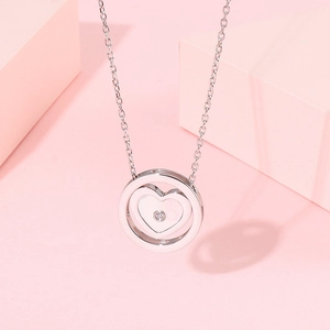Détail d'un collier pendentif cœur argenté avec zircon brillant sur fond rose pastel