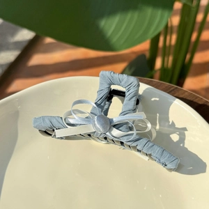 Detail of light blue striped fabric bow hair claw clip displayed on a white ceramic plate