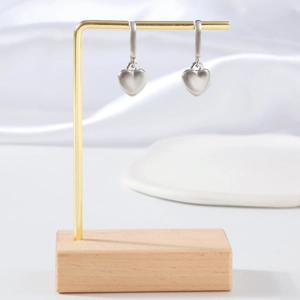 Minimalist silver heart earrings on a gold metal stand with a wooden base display