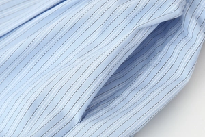 Macro shot of light blue striped shirt fabric showing precise side pocket stitching detail