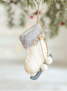 Close-up of knitted white Christmas ice skate ornament hanging on a pine branch with berries