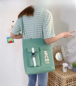 Detail of green canvas tote bag featuring functional front pockets and bold letter print
