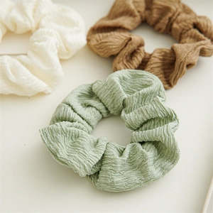 Detail of polyester fabric scrunchies in cream, khaki, and green showing pleat texture
