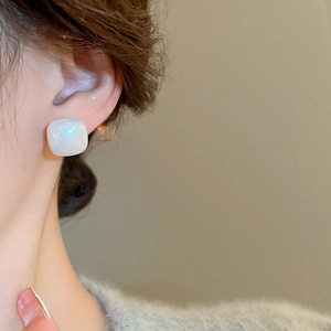 Close-up of square pearl studs with golden plating worn on ear for an elegant look