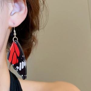 Detailed close-up of acrylic butterfly wing earrings with red and black patterns on a model